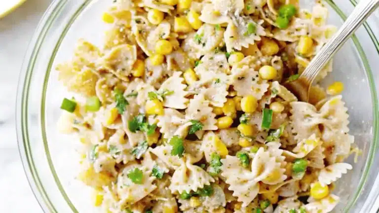 Elote pasta salad in a bowl, garnished with cotija cheese, lime wedges, and cilantro, served on a rustic wooden table.